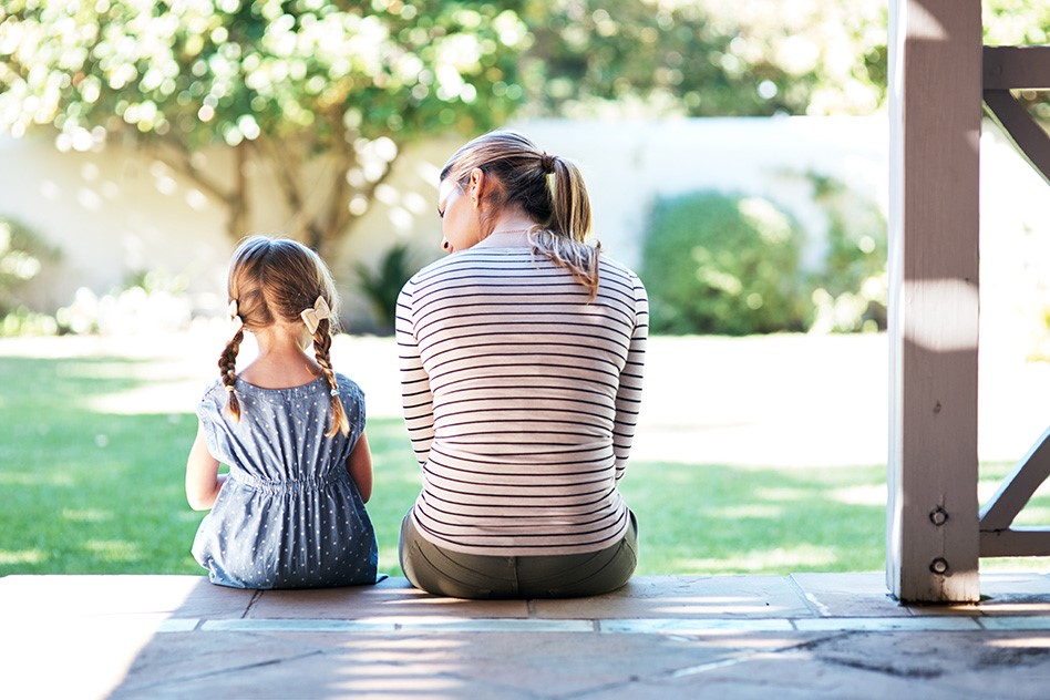 Mother and young daughter sat on a porch